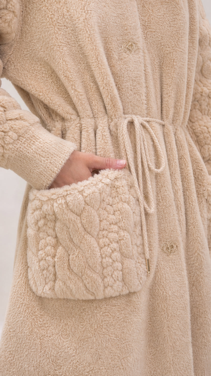 Close-up detail of beige fleece coat showing cable-knit pocket and waist drawstring