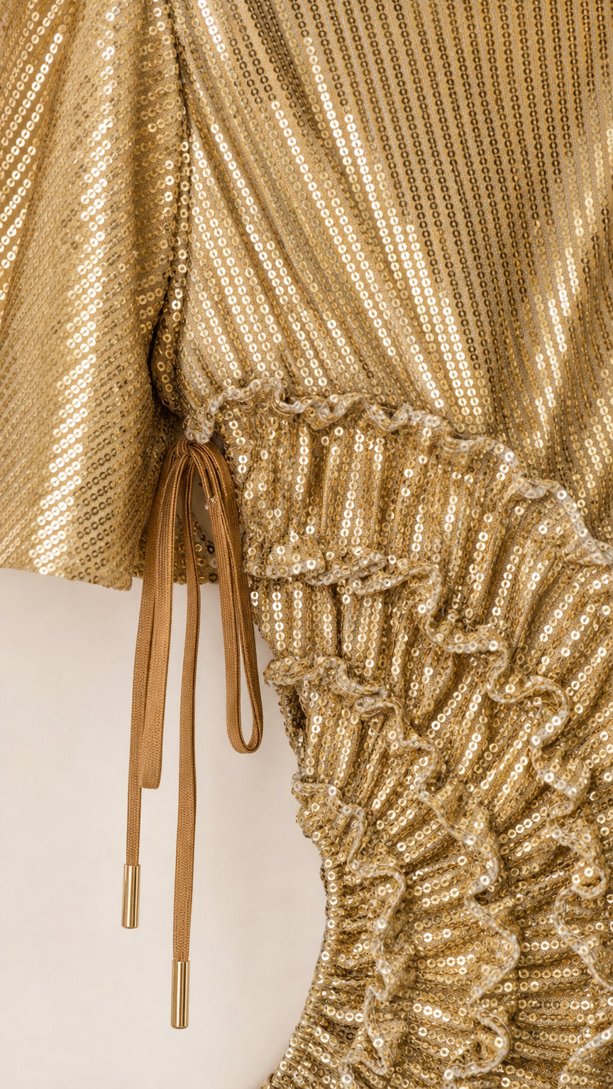 Close-up detail of the gold sequin fabric texture, ruffled waist cutout, and drawstring