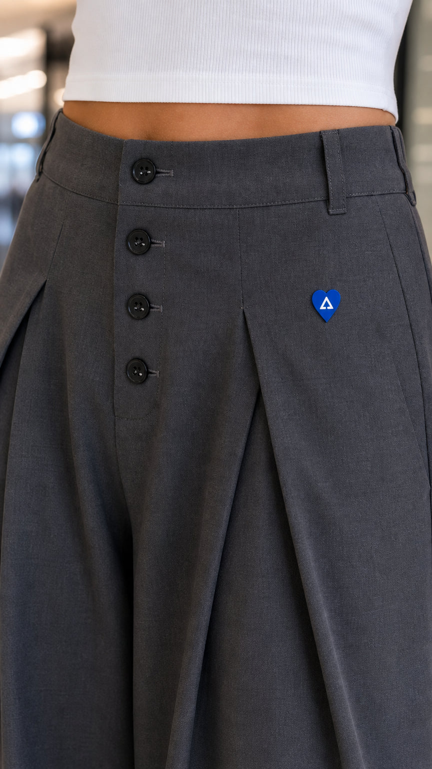 Close-up detail of high-rise front button placket and pleats on charcoal grey trousers