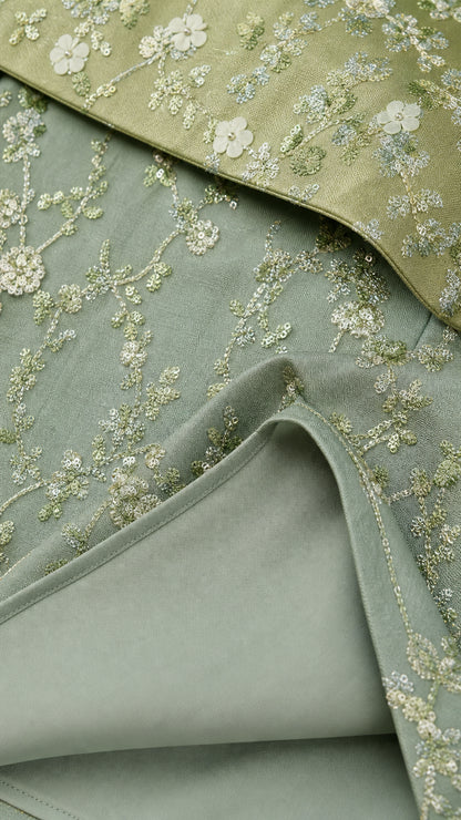 Close-up detail of floral embroidery and hem on sage dress