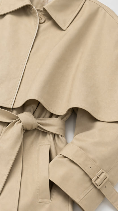 Close-up detail of beige trench coat lapel, fabric belt, and buckled sleeve cuff