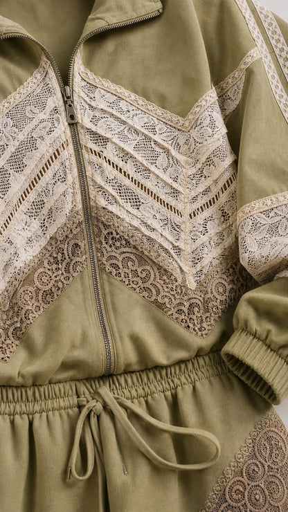 Close-up detail of zipper, collar, and geometric lace inserts on sage green jacket