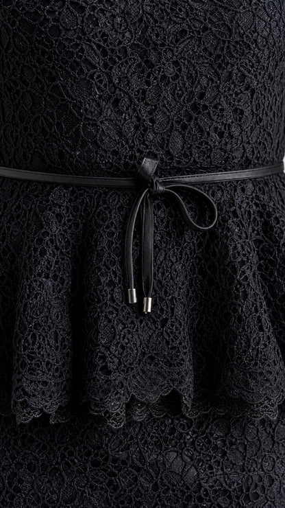 Close-up detail of black lace fabric, peplum frill, and slim tie belt