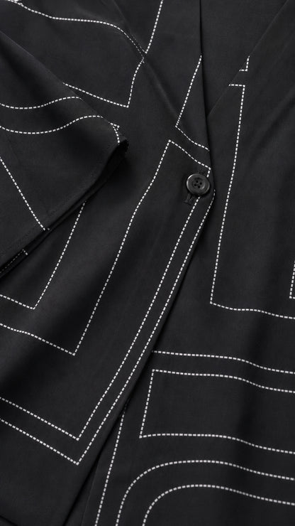 Close-up detail of white geometric line print and button closure on black fabric