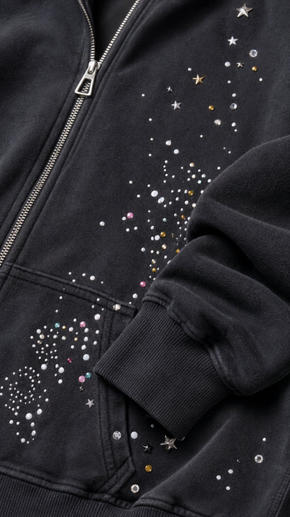 Close-up detail of rhinestone studs, star embellishments, and zipper on black hoodie pocket