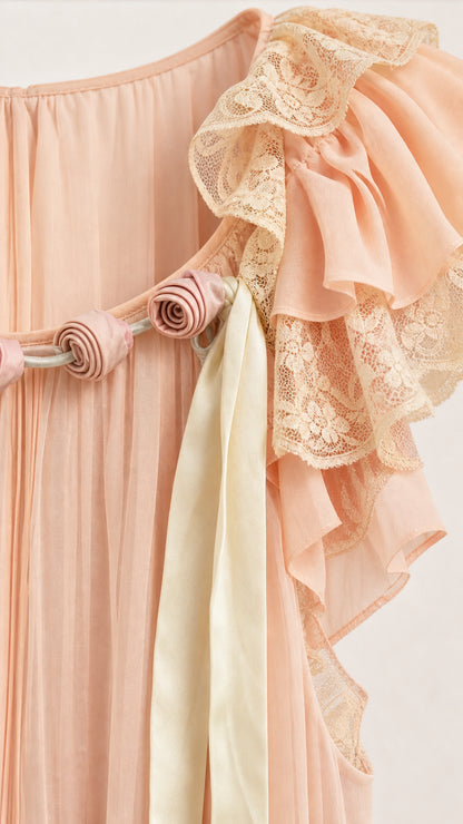 Close-up detail of blush pink pleated fabric, lace ruffle trim, fabric rose rosettes, and satin ribbons