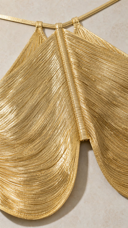 Close-up detail of textured metallic pleating on gold halter top