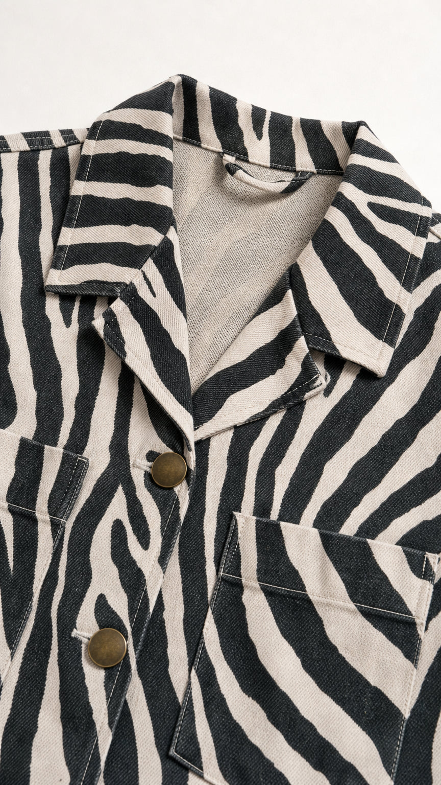 Close-up detail of textured fabric, notch collar, buttons, and pocket on zebra print shirt