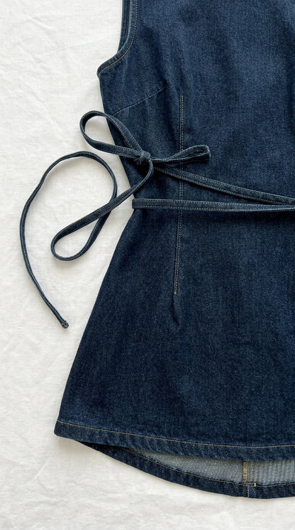Close-up flat lay detail of dark blue denim dress side waist tie and hem