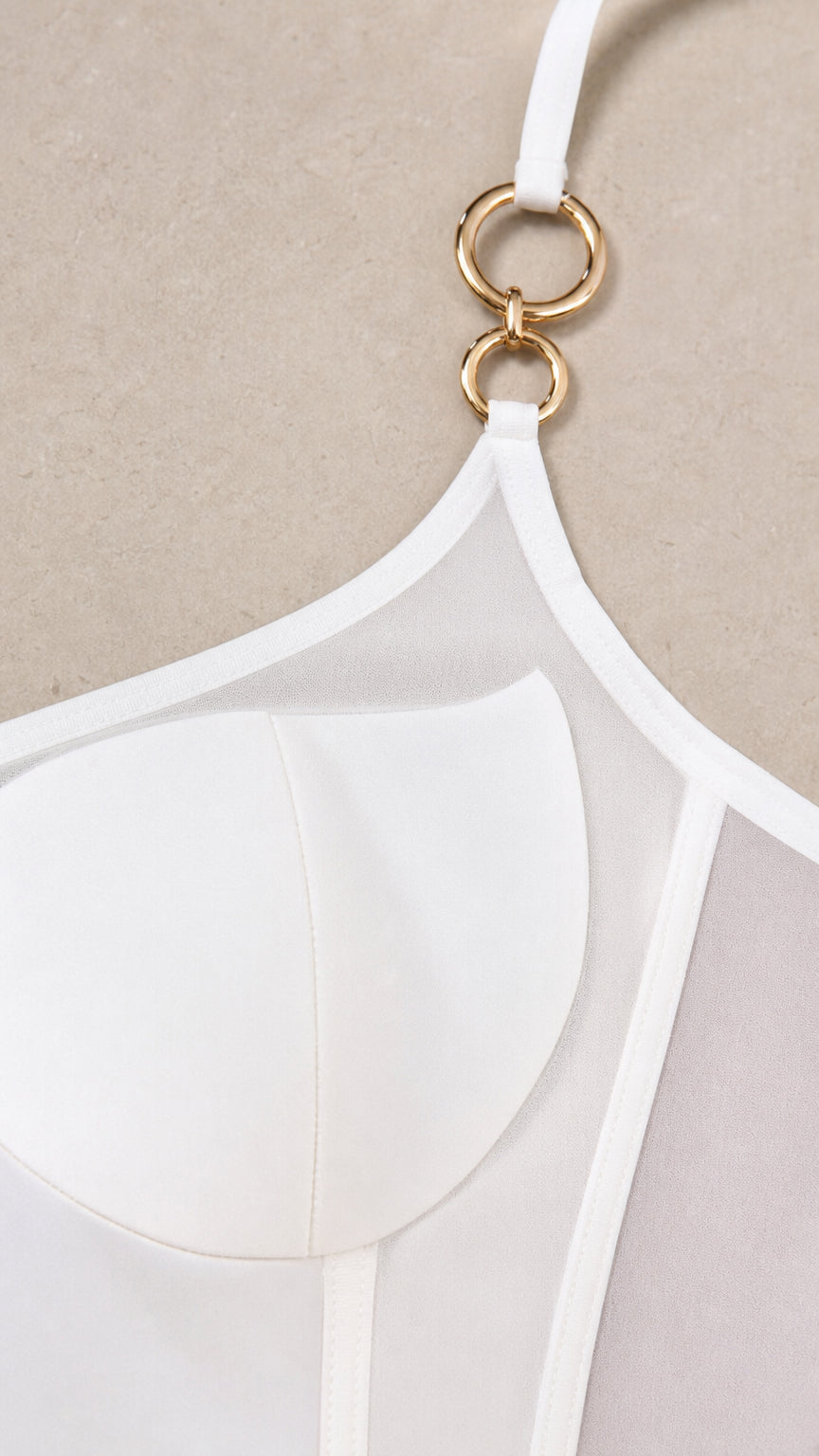 Close-up detail of white dress bodice showing gold-tone interlocking rings and sheer mesh cups