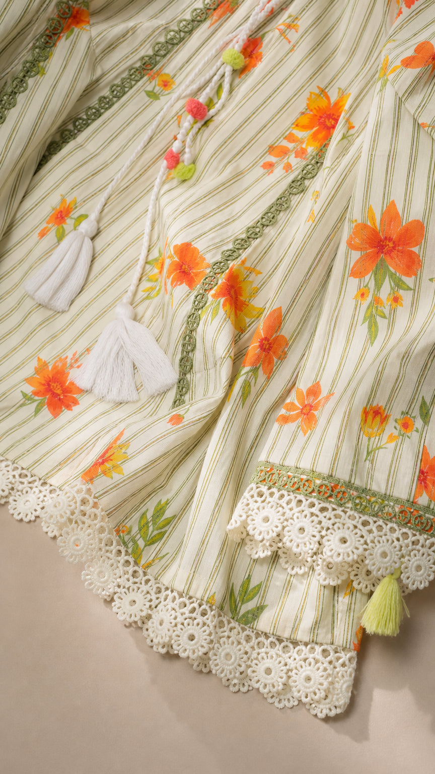 Close-up detail of floral pattern, tassel ties, and lace hem