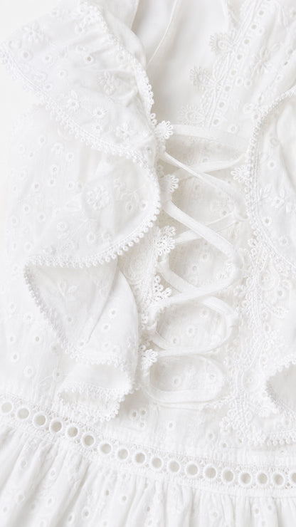 Close-up detail of white eyelet embroidery, ruffle trim, and side lace-up ties