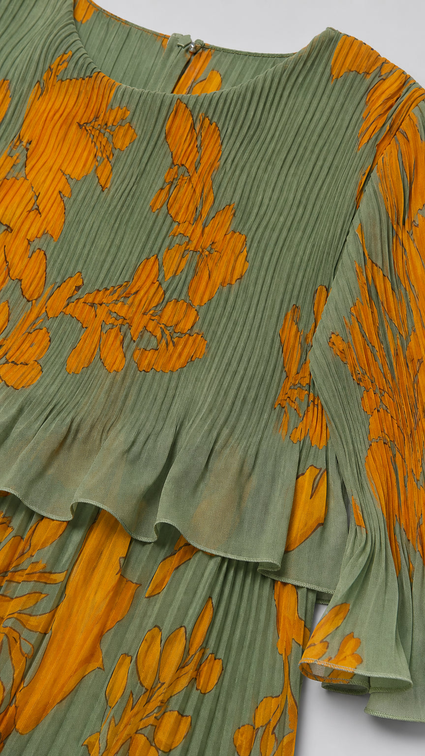 Close-up detail of accordion pleating, crew neckline, and ruffle hem on sage green floral fabric