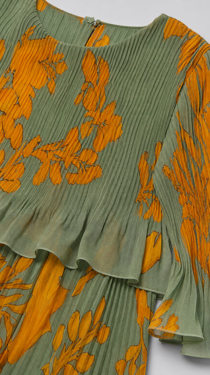 Close-up detail of accordion pleating, crew neckline, and ruffle hem on sage green floral fabric