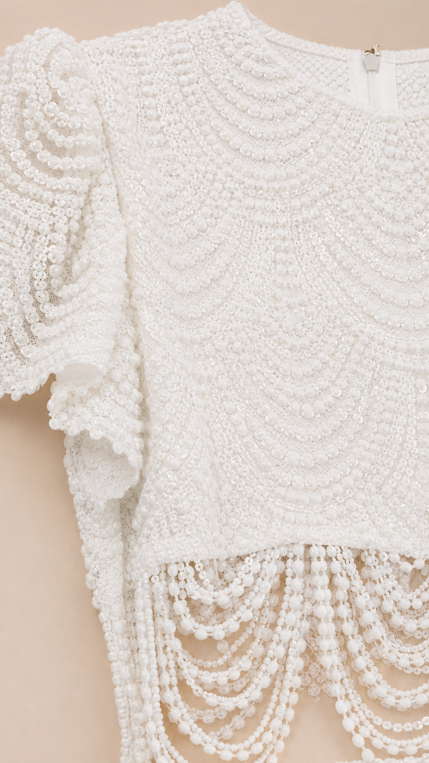 Close-up detail of the intricate beadwork and fringe hem on white top