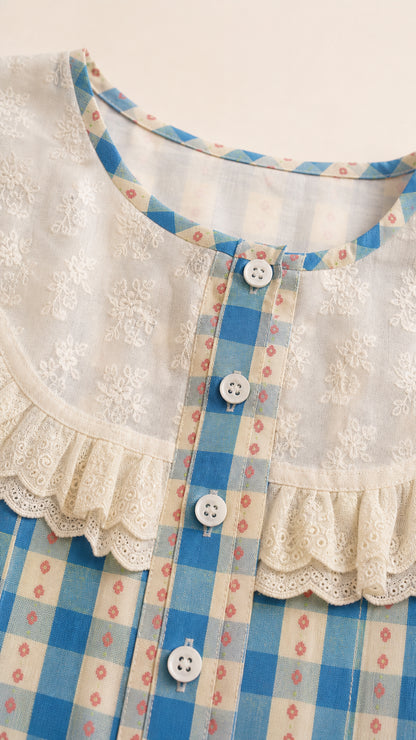 Close-up detail of white embroidered lace collar, buttons, and blue plaid fabric