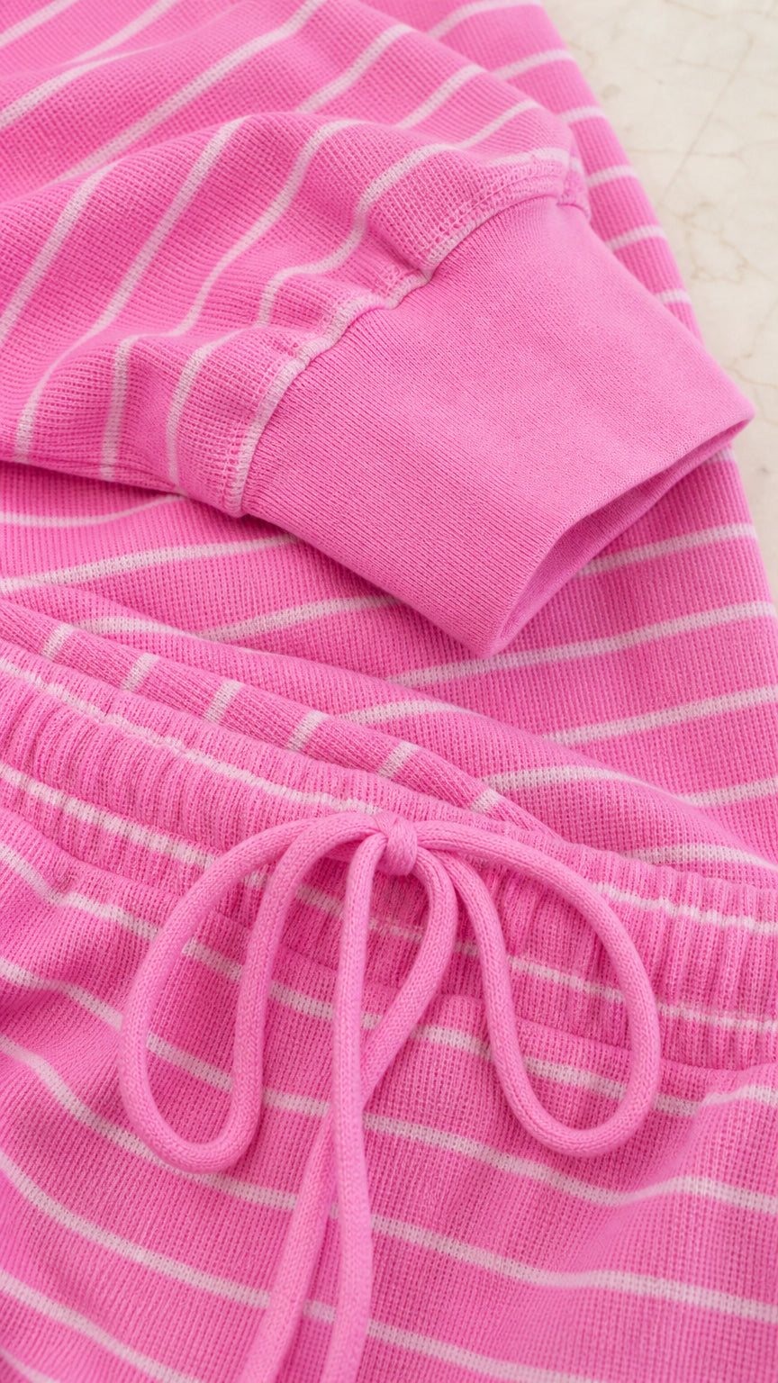 Close-up detail of pink striped waffle knit fabric, ribbed sleeve cuff, and drawstring waistband