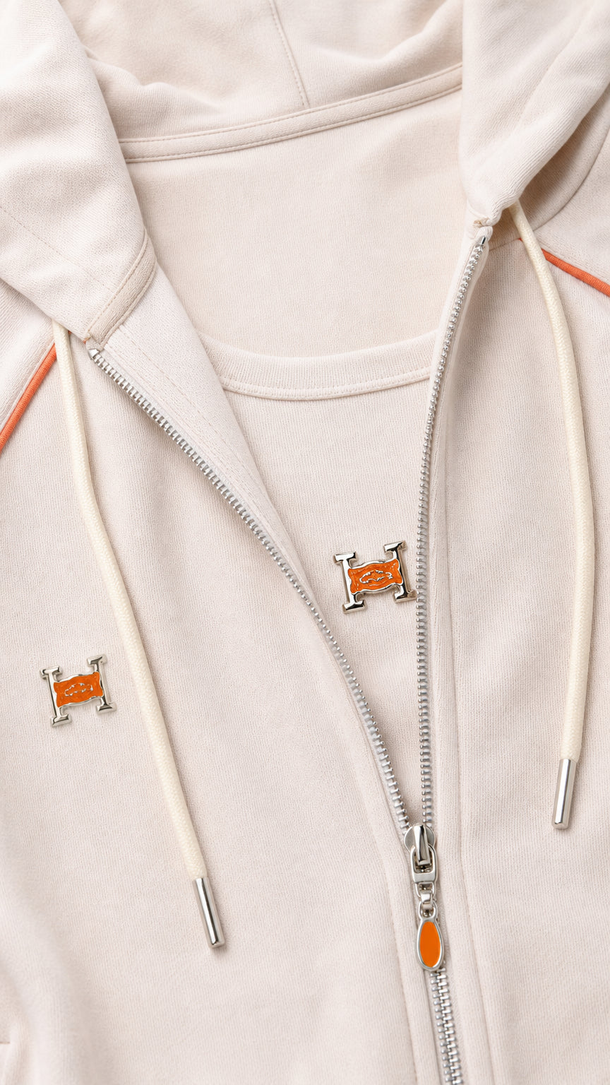 Close-up detail of beige zip hoodie with contrast orange piping and metallic zipper hardware