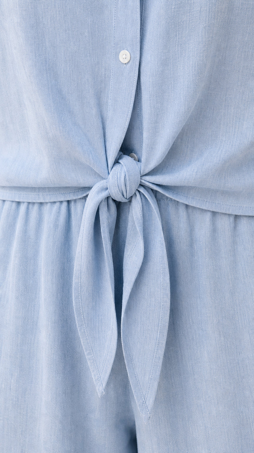 Closeup of tie waist and button placket on light blue jumpsuit