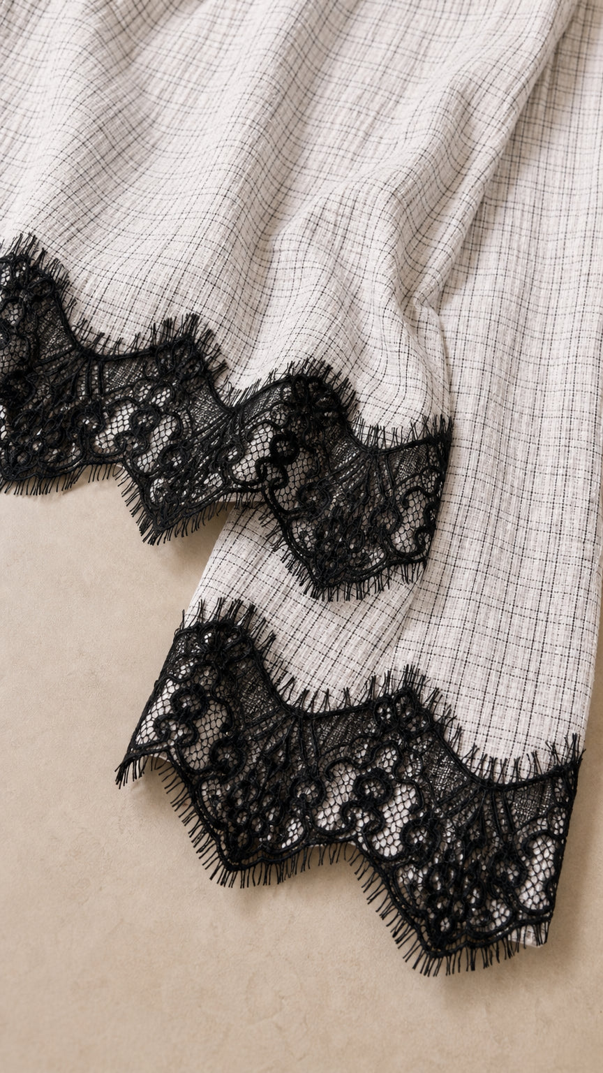 Close-up of textured white plaid fabric and scalloped black lace trim