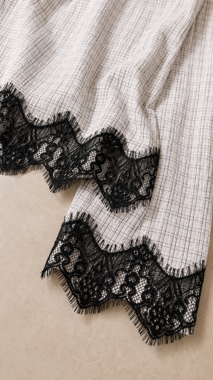 Close-up of textured white plaid fabric and scalloped black lace trim