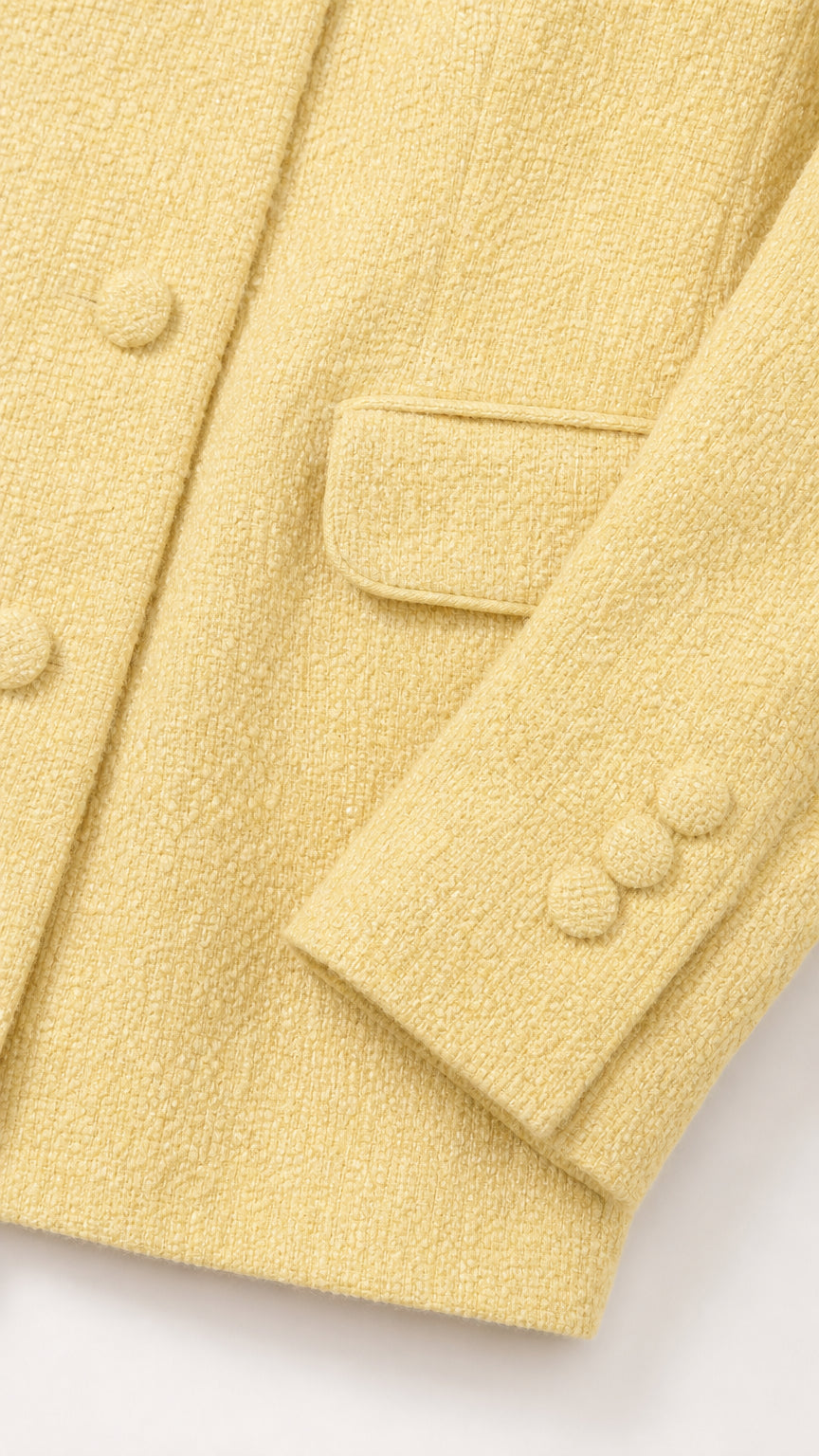 Close-up detail of textured pastel yellow tweed fabric showing covered buttons and pocket flap