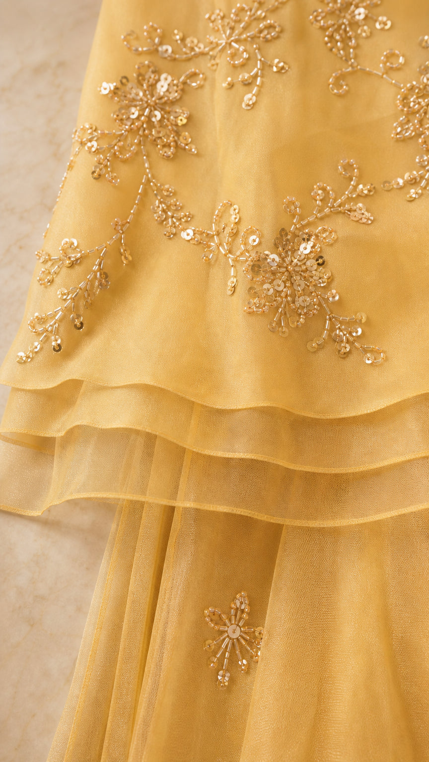 Close-up detail of sheer tiered fabric with floral sequin vine embroidery