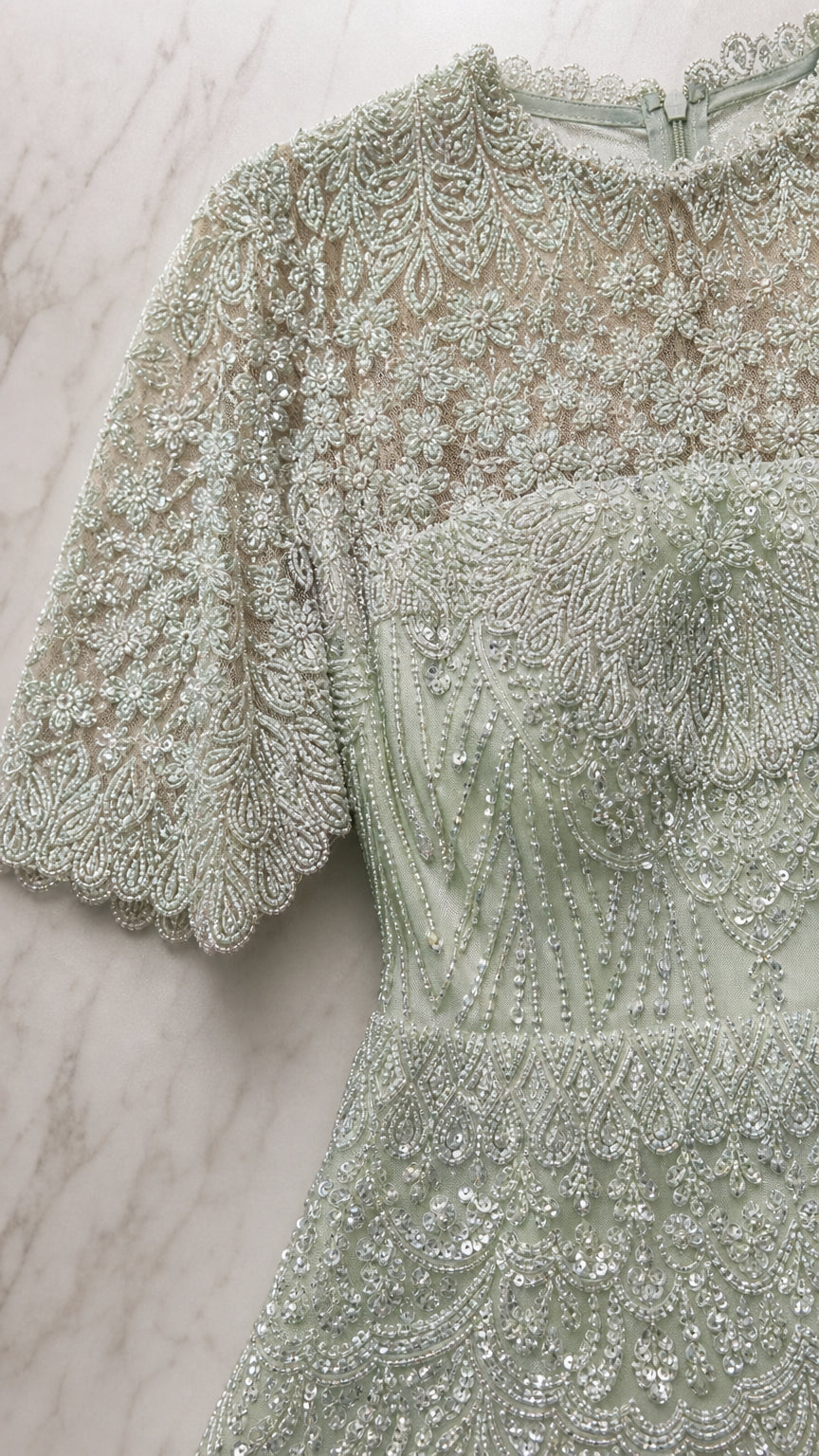 Close-up detail of intricate beadwork, sheer neckline, and scalloped sleeves on sage green dress