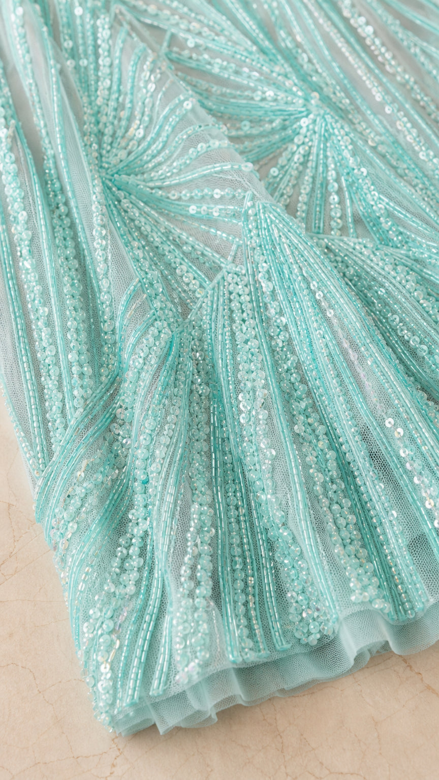 Close-up detail of shimmering sequin and bead embroidery on aqua blue tulle fabric