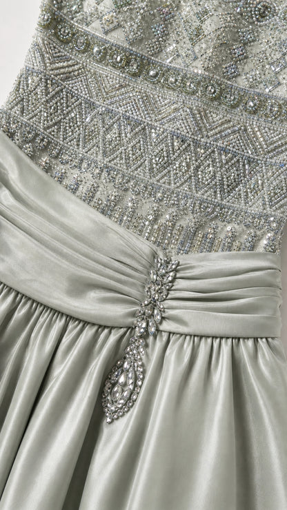 Close-up detail of intricate beadwork, pleated waist, and crystal brooch accent