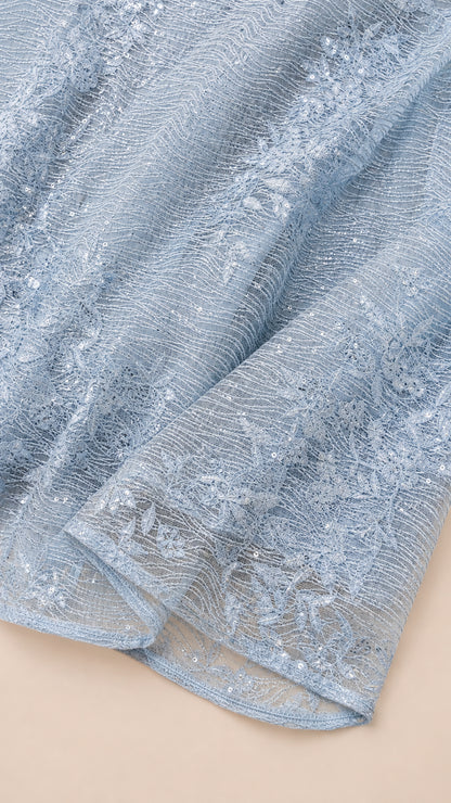 Close-up detail of textured light blue lace fabric with embroidery and sequins
