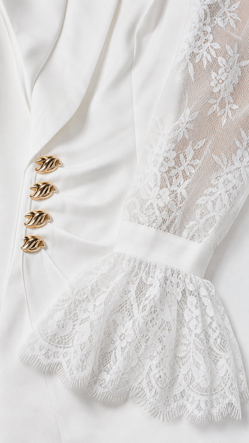 Close-up detail of white blazer showing sculptural gold buttons and sheer floral lace sleeve