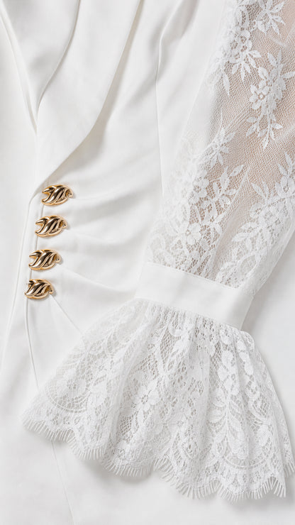 Close-up detail of white blazer showing sculptural gold buttons and sheer floral lace sleeve