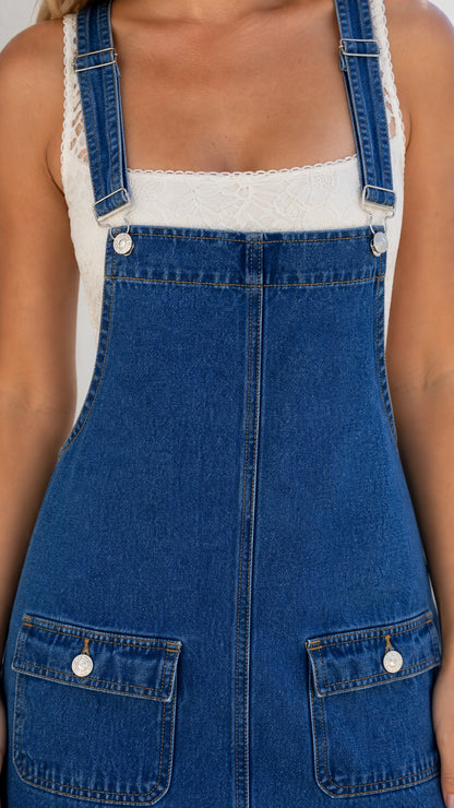 Close-up detail of straps, buttons, and front pockets on blue denim overall dress
