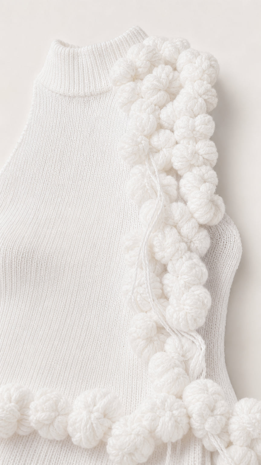 Close-up detail of white ribbed knit fabric and textural yarn pom pom trim