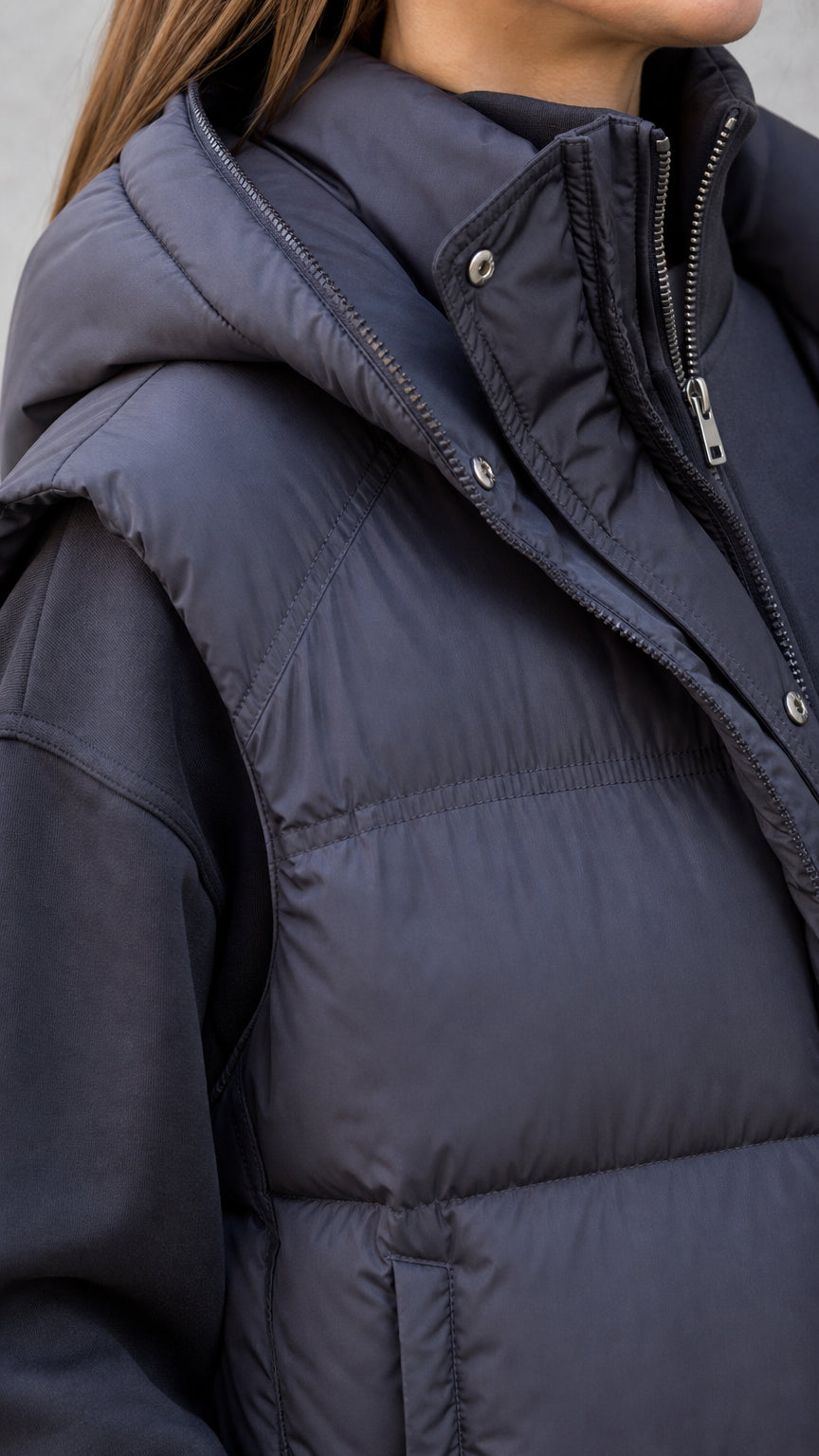 Close-up detail of black hooded puffer vest showing collar and zipper closure
