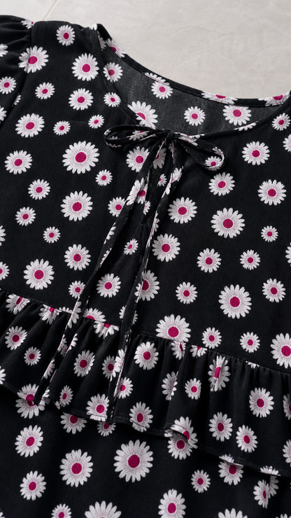 Close-up detail of keyhole tie neckline and ruffle trim on black daisy print top