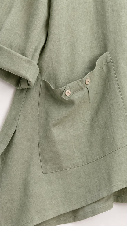 Close-up detail of tunic asymmetric hem and button pocket in sage green