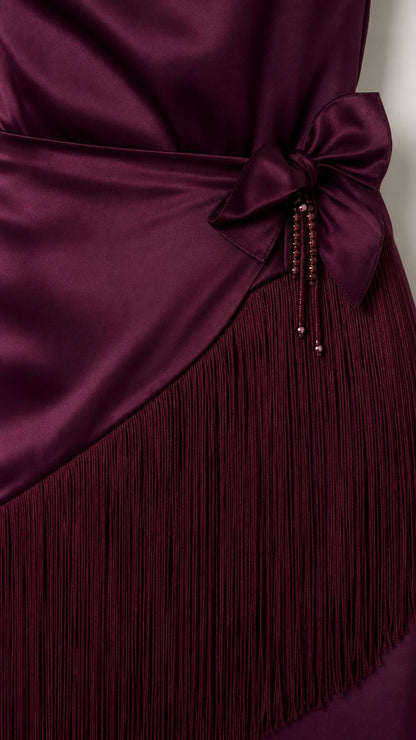 Close-up of waist bow detail and fringe hem on burgundy dress