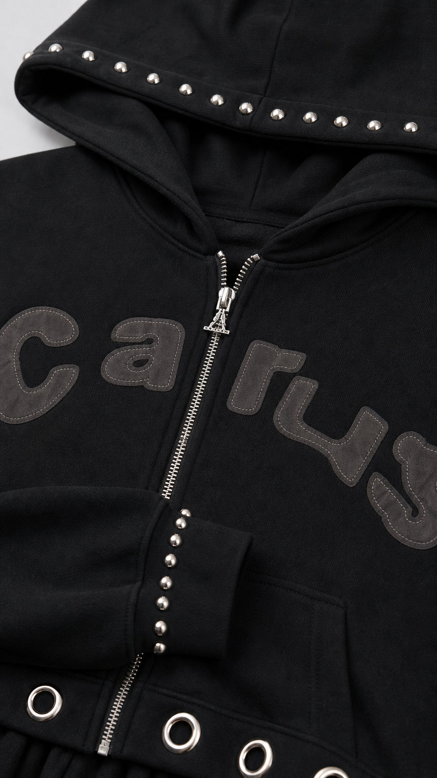 Close-up detail of black zip hoodie showing hood studs, sleeve studs, and hem grommets