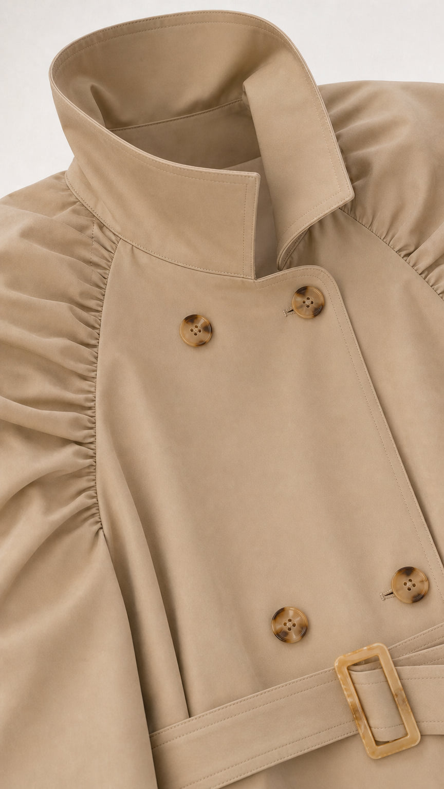 Close-up detail of beige trench coat lapel, tortoiseshell buttons, and gathered shoulder