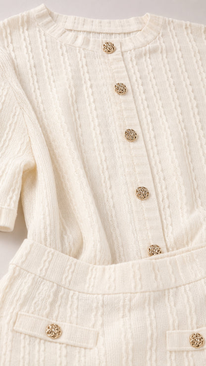 Close-up detail of cream textured knit fabric, round neckline, and gold-tone buttons
