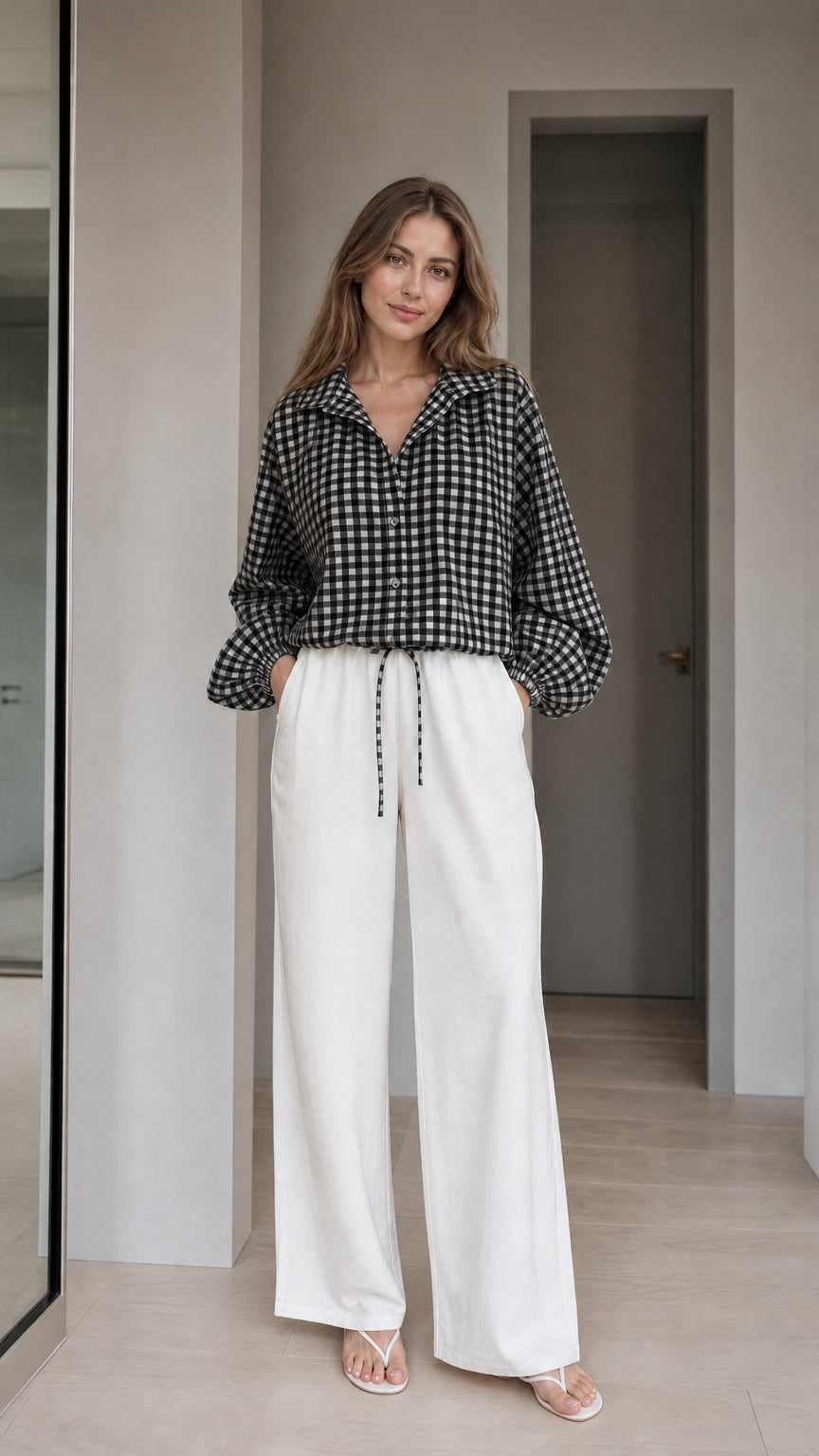Woman wearing black gingham check blouse and white wide-leg trousers, front view