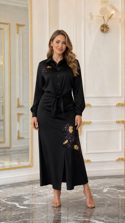 Woman wearing a black satin-look embroidered maxi shirt dress with tie waist