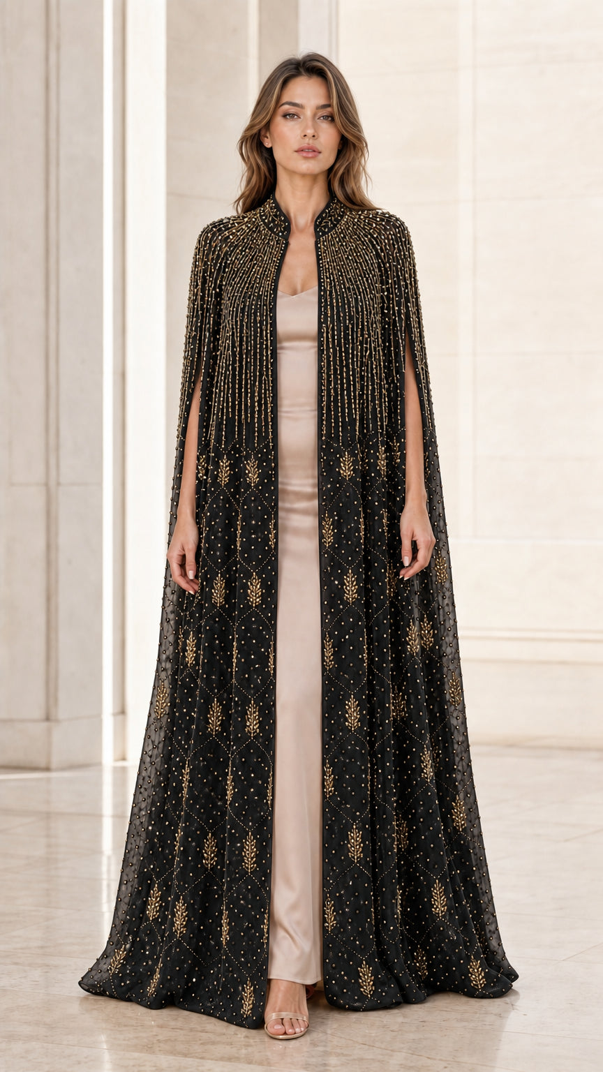 Model wearing black floor-length beaded cape evening gown with gold accents