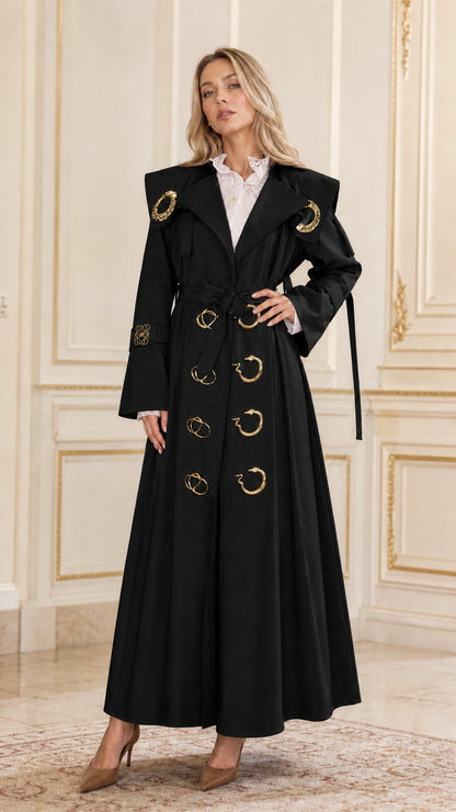 Front view of woman wearing black maxi belted trench coat with gold accents