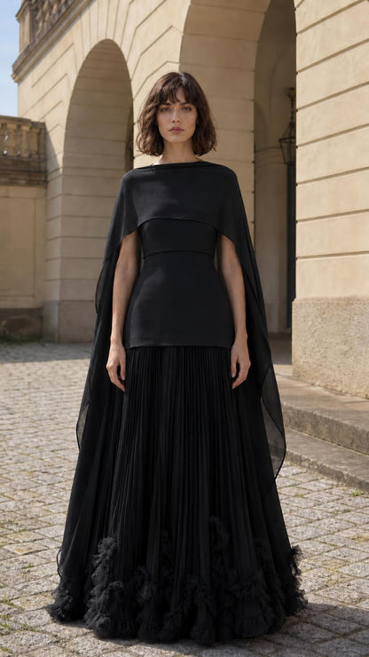 Front view of woman wearing black cape overlay pleated maxi dress