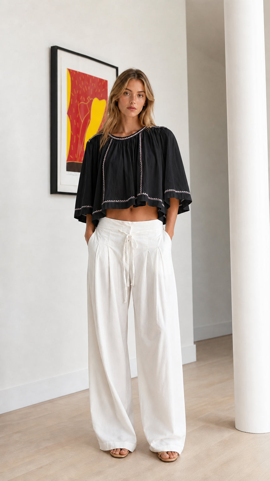 Front view of black embroidered cropped swing blouse paired with white wide-leg pants