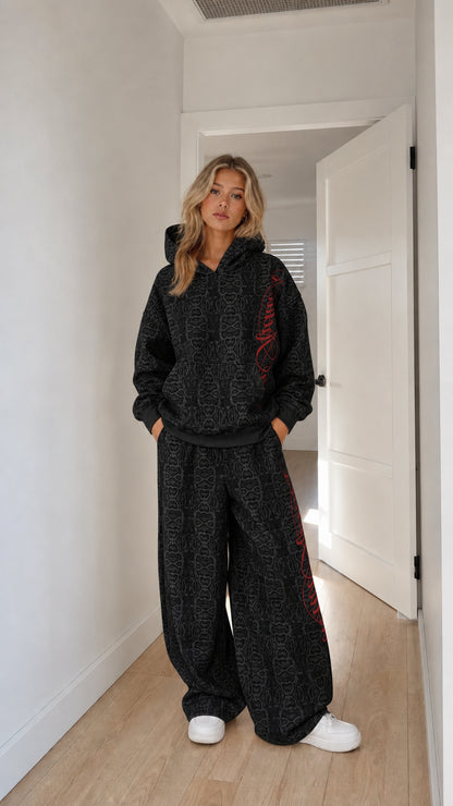 Model wearing black embossed monogram hoodie and wide-leg tracksuit set