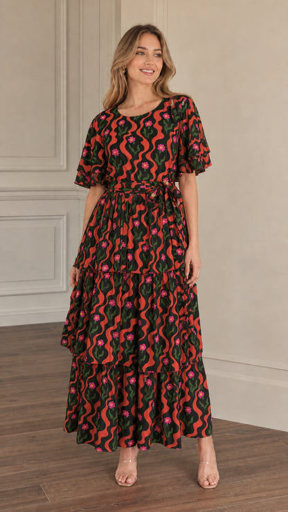 Front view of model wearing black floral wave print tiered maxi dress